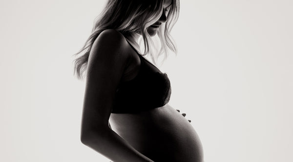 Foto del profilo di una donna incinta in biancheria intima. ©Janko Ferlic per Unsplash.