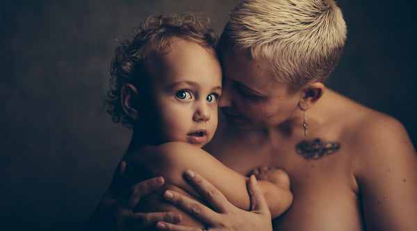 Donna nuda a torso nudo che tiene il suo bambino pelle a pelle ©Janko Ferlic per Unsplash. 
